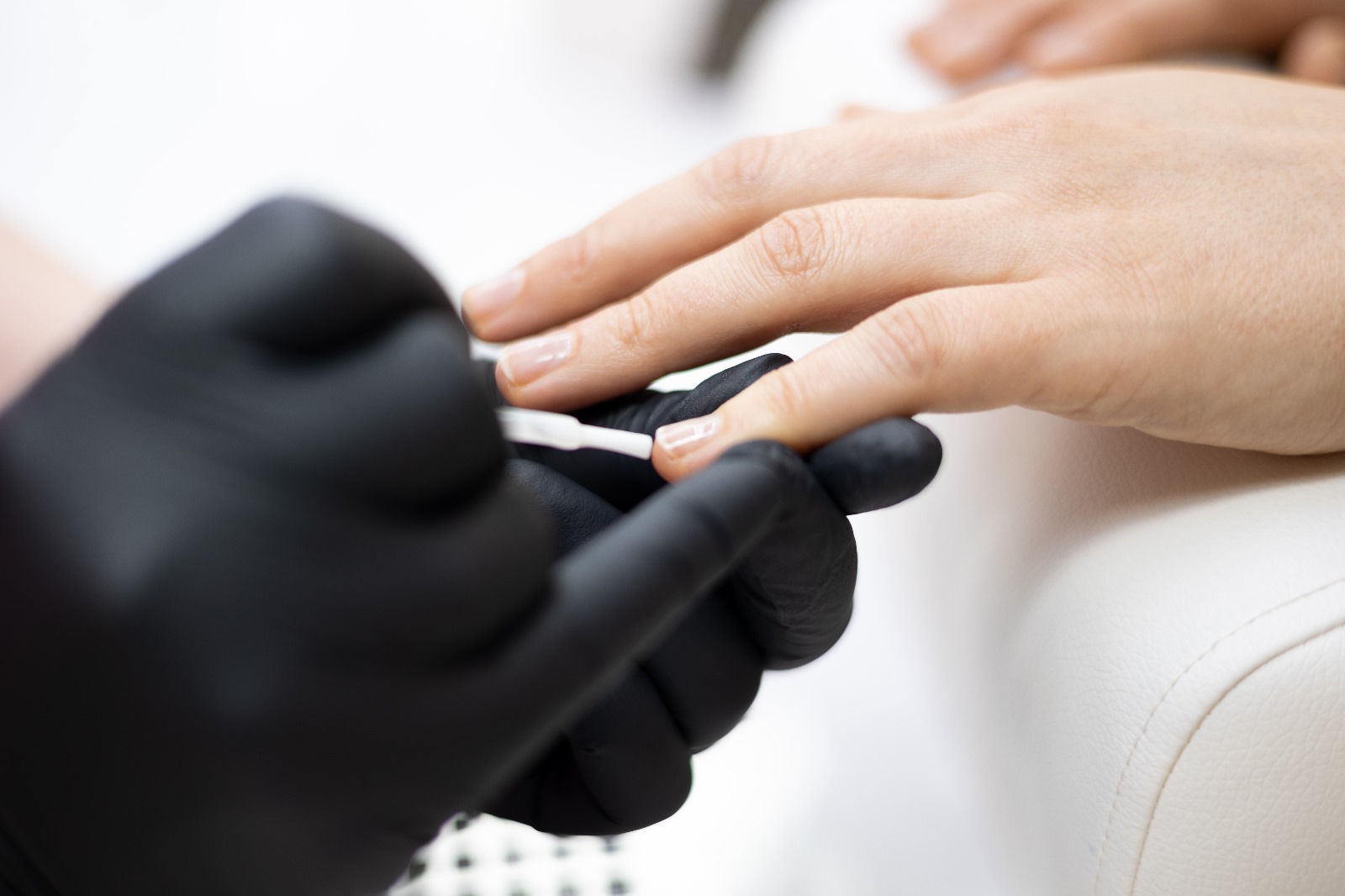 Manicure dłoni klientki w czarnych rękawiczkach - strony internetowe dla kosmetyczek